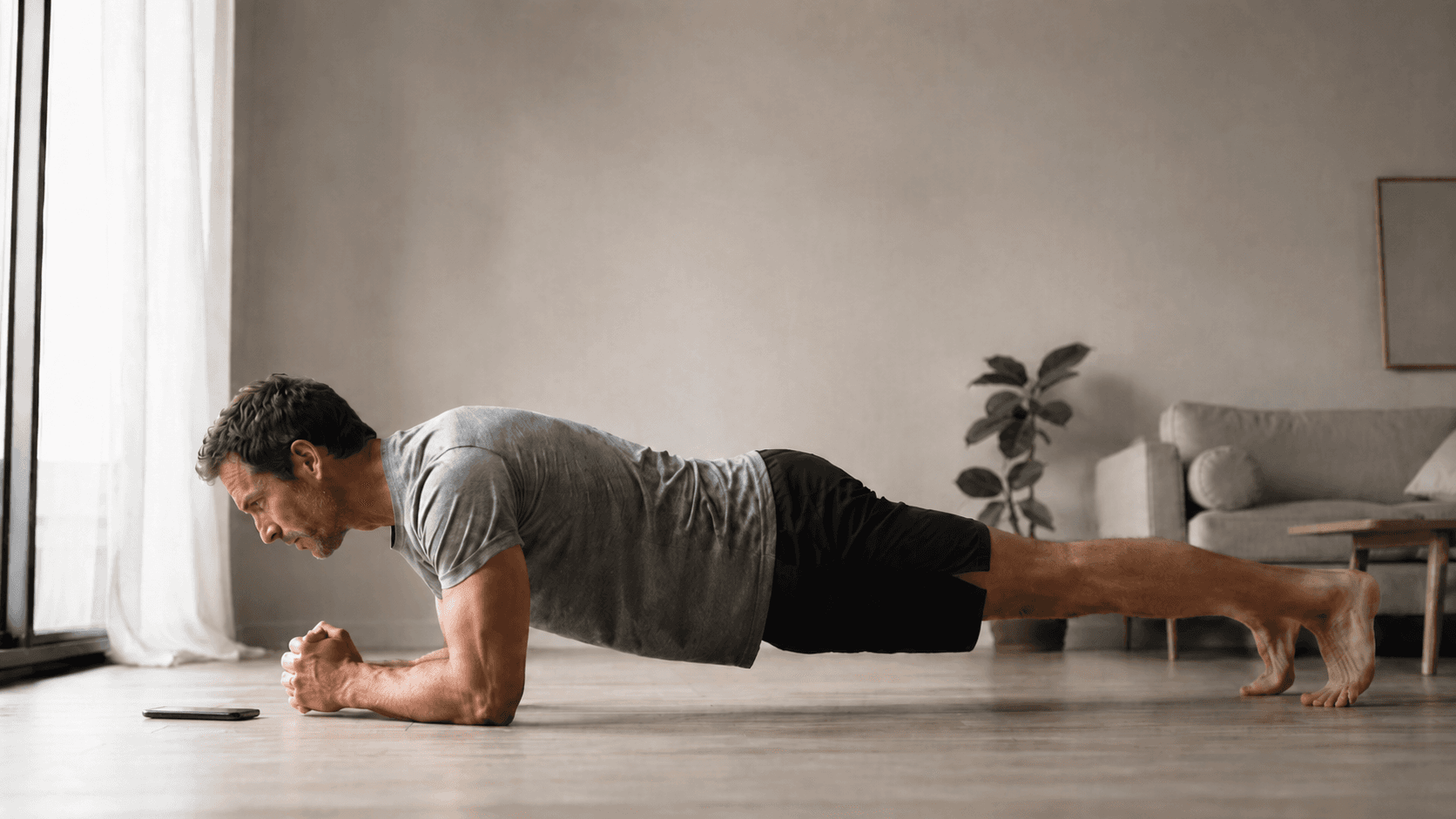Man holding a forearm plank on the floor of a bright living room with a phone beside him