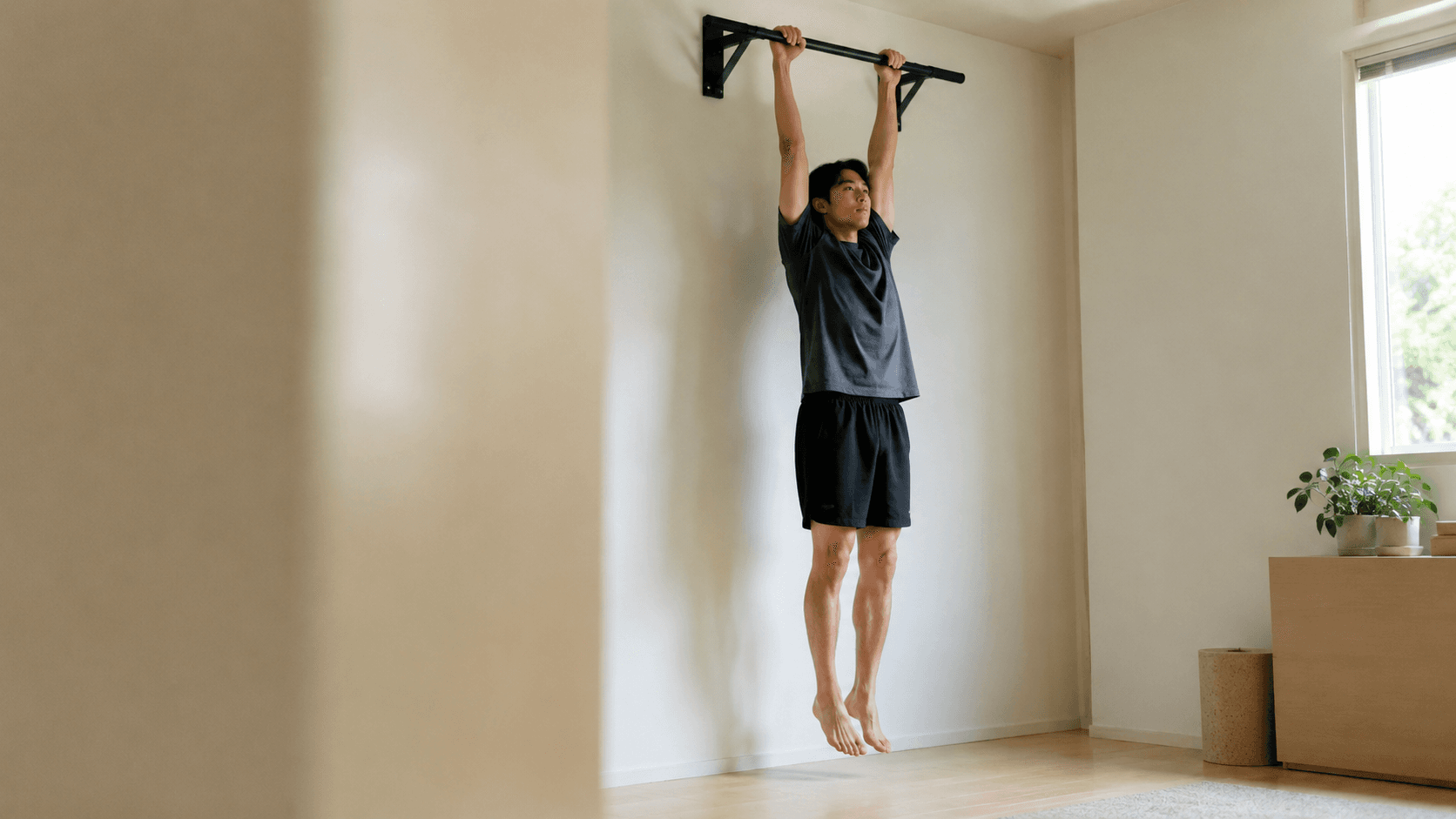 A man doing a relaxed dead hang from a wall-mounted pull-up bar in a bright, minimal home room